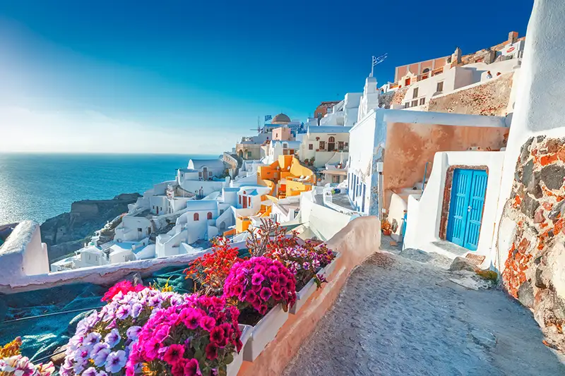 The same coastal village seen after cataract surgery: sharp and clear, with crisp white walls, vivid flowers and blue sea